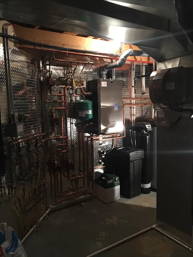Basement mechanical room with copper heating lines running to a boiler and water treatment equipment