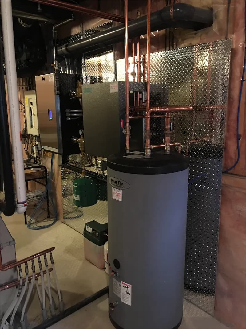 Hot water storage tank in front of a wall-mounted boiler and copper distribution piping