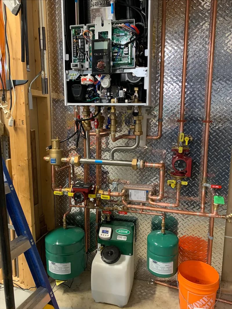A combination boiler with its cover removed, showing internal controls above copper piping and expansion tanks