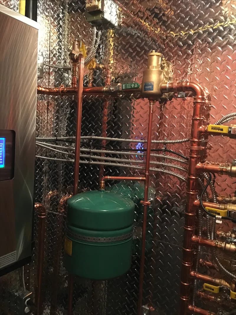 Green expansion tank and copper piping connected to a boiler in a mechanical room