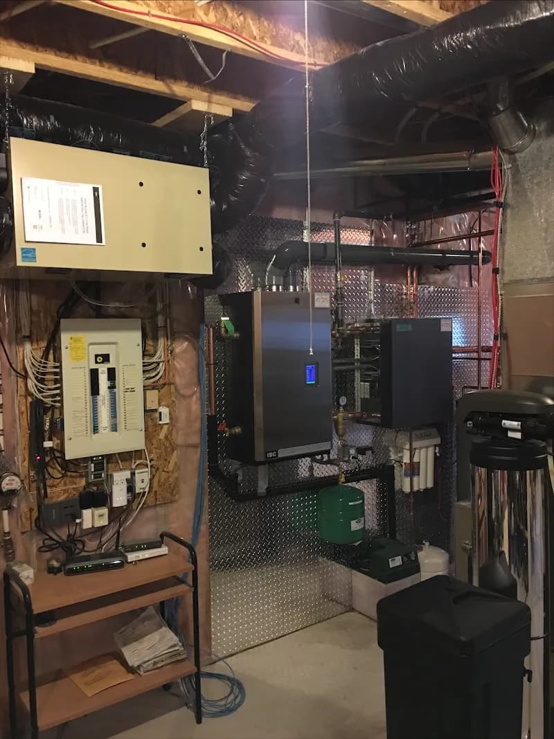 Electrical panel and boiler controls mounted beside copper heating piping in a basement mechanical room