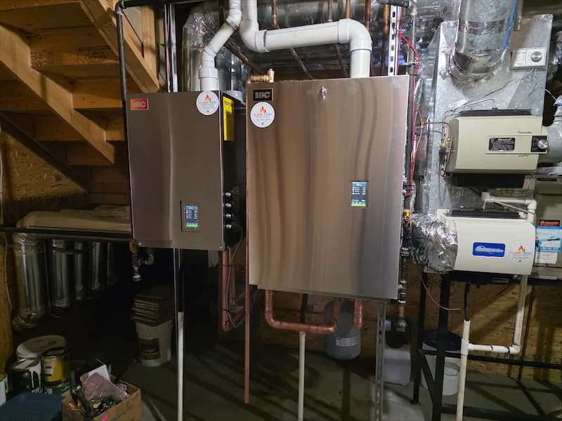 Two wall-mounted boilers with flue venting and copper supply lines in a basement mechanical room