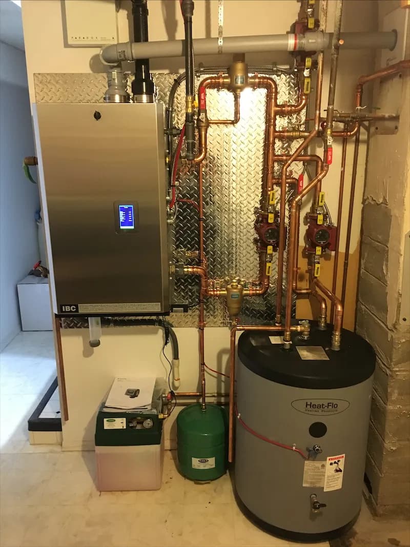 Stainless boiler and hot water storage tank connected by copper piping in a residential utility room
