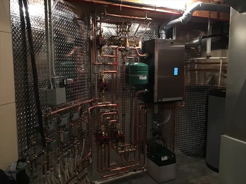 Copper manifold and expansion tank feeding a wall-mounted boiler, with heating ductwork overhead