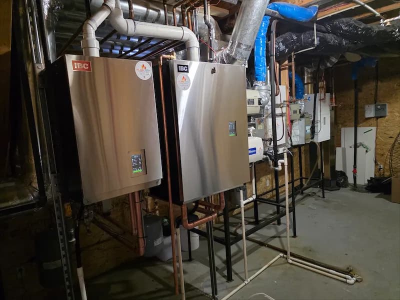 Two wall-mounted boilers installed side by side with copper piping and venting in a basement
